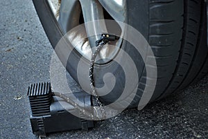 Close up of a portable air compressor connected to the valve stem of a car tire