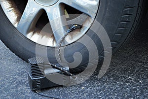 Close up of a portable air compressor connected to the valve stem of a car tire