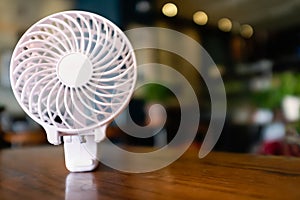 Close up of a portable battery operated fan, folded on a wooden table. The inner part is spinning with motion blur.