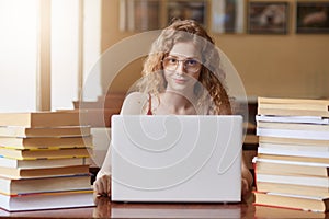 Close up portait of teenage girl studying and using new technologies, sitting at table in front of opened white lap top, lady