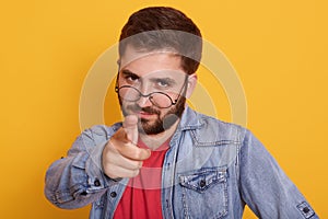 Close up portait of young caucasian man dresses red t sirt and denim jacket, pointing at camera, chhosing something, bearded guy
