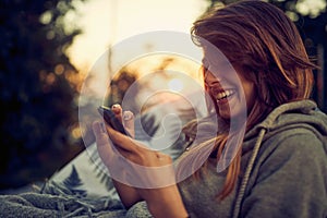 Close up portarit shot of beautiful joyful young woman using smartphone, enjoying her time outdoors, sitting in cozy chair photo