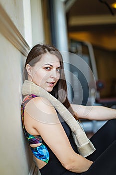 Close up portrait of adorable charming smiling young fitness girl with towel and posing while looking at camera in gym