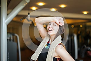 Close up portrait of adorable charming smiling young fitness girl with towel and posing while looking at camera in gym