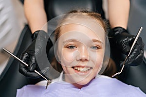 Close-up portrait of adorable little girl smiling looking at camera sitting in stomatology seat while pediatric dentist