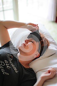 Close up portrait of Adult beautiful caucasian woman sleeping in white bed with gray eye mask