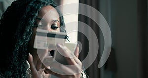 Close up portrait of an African American female with curly hair holding a smartphone and credit card while shopping