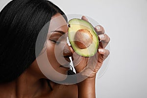 Close-up portrait of afro young woman with avocado, healthy lifestyle. Posing over white background.