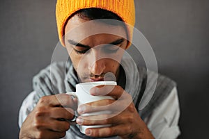 Close-up portrait of alone sitting young handsome man with a mug of coffee, tea, water, on gray background.