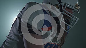 Close up portrait american football sportsman player in football helmet holding he ball and preparing to run on black