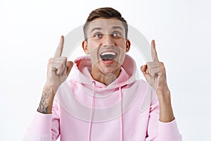 Close-up portrait of amused, rejoicing handsome blond guy in pink hoodie, look up with joyful amazed smile, looking at