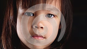 Close-up portrait of an angry cute little girl looking at camera with regret and displeasure in her eyes in the dark room at home.