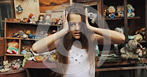 Close-up portrait of the angry little girl with long dark hair nerveously touching her head and almost shouting. Garden