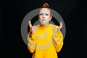Close-up portrait of angry mad young woman in yellow sweater screaming on isolated black background