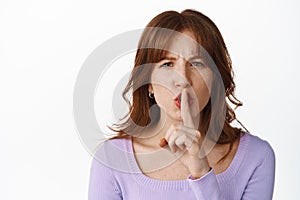 Close up portrait of angry shushing girl, say shhh and frowning, press finger to lips, taboo dont speak gesture, telling