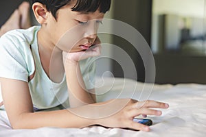 Close up portrait of Asian boy with black bangs, black eyes with a smiling face wearing a light green shirt lying on the bed in