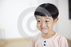 Close-up portrait Asian child boy straight black hair wearing a light brown shirt looking at camera of him make funny faces of