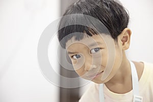 Close-up portrait Asian child boy straight black hair wearing a white shirt looking at camera of him make funny faces of happy