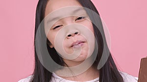 Close up portrait of asian girl eating chocolate, biting whole bar and enjoying it, pink studio background