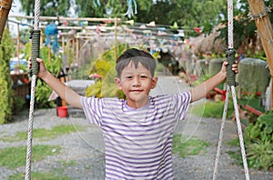 Close-up portrait of Asian little boy child spread arms out and hold tight onto the rope while standing on swing in the garden