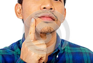 A close up portrait of an Asian man is touching his own chin in blue plaid shirt