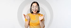 Close up portrait of asian woman looking surprised, wow face, staring impressed at camera, standing over white