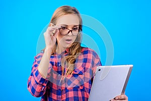Close up portrait of astonished pretty cute charming with long blonde hair shocked teenager touching glasses looking at tablet in