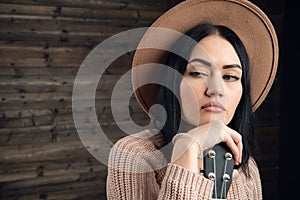 Close up portrait of an attractive brunette woman wearing sweather and hat with beautiful guitar. Wooden background