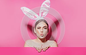Close-up portrait of attractive cheerful girl wearing pink ears, air kiss. Easter bunny woman.