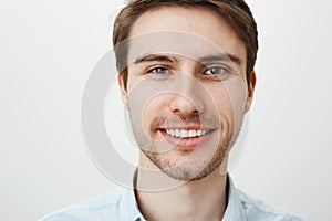 Close-up portrait of attractive confident adult male with bristle smiling broadly while looking at camera, standing