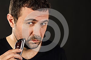 Close up portrait of an attractive Eatsern European man trimming his beard. Black background with copy space