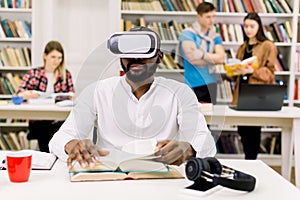 Close up portrait of attractive focused young african american bearded student sitting in library and reading book in vr