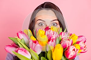 Close-up portrait of attractive funny amazed girl holding bunch tulips hiding isolated over pink pastel color background