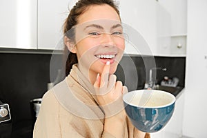 Close up portrait of attractive girl drinking coffee, holding cup with morning cappuccino and smiling, having a mug of