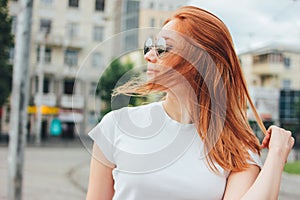 Close up portrait of attractive redhead smiling girl in sunglasses in casual clothes at street in city