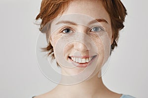 Close-up portrait of attractive redhead woman with cute freckles and clean perfect skin, smiling broadly, being in good