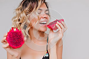 Close-up portrait of attractive tanned woman with short hairstyle eating dragon fruit. Studio shot