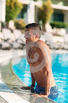 Close up portrait of attractive young man resting on edge of swimming pool