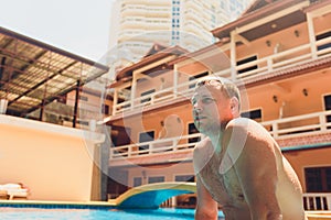 Close up portrait of attractive young man in sunglasses resting on edge of swimming pool.