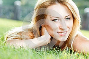 Close up portrait of an attractive young woman laying down on green grass in a park during the summer and listening to