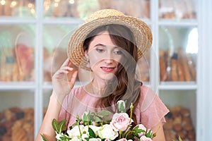 Close-up portrait of an attractive young woman in a summer dress and straw hat, holding a bouquet of flowers against a background