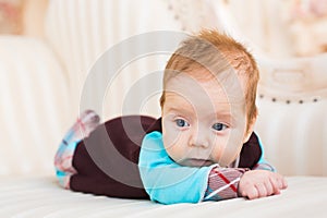 Close-up portrait of baby boy with red hair and blue eyes. Newborn child lyling in couch.