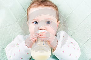 Close up portrait of a baby girl with a milk bottle lying on a green knitted blanket