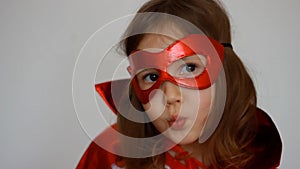 Close up portrait baby girl plays superhero. Funny child in a red raincoat and mask playing power super hero. Superhero