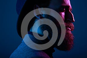 Close up portrait of a bearded man in hat and suit, with close eyes posing in profile, on dark blue background.