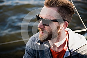 Close up portrait Bearded man model wearing sunglasses and hoodie looks away, sunset in the sea scenery.