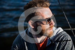 Close up portrait Bearded man model wearing sunglasses and hoodie looks away, sunset in the sea scenery.