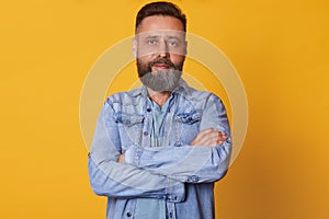 Close up portrait of bearded middle aged confident man with folded arms, standing straight, having serious facial expression,