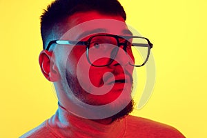 Close Up portrait of bearded scared young guy, student isolated on yellow background in red color light, filter. Fears
