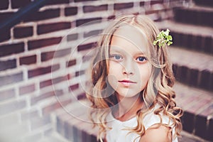 Close-up portrait of beautiful 9 -10 years old girl with blond curly hair sitting on the stairs.